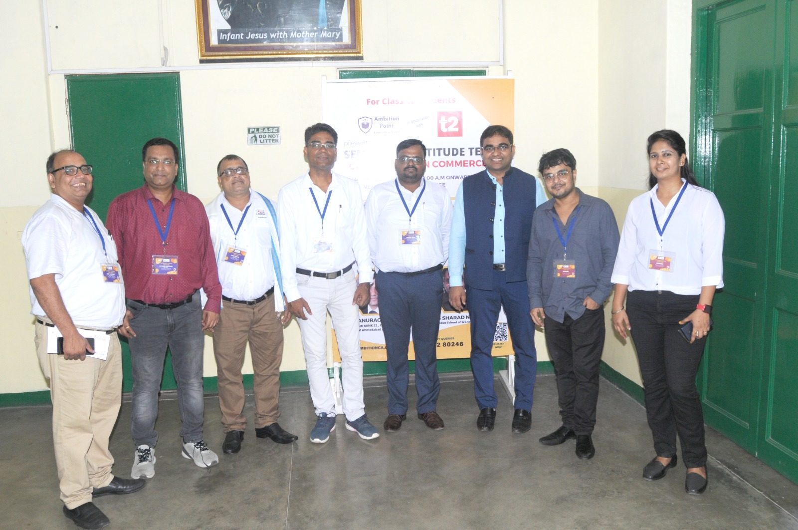 Eight facilitators with lanyards standing in front of an aptitude test event banner