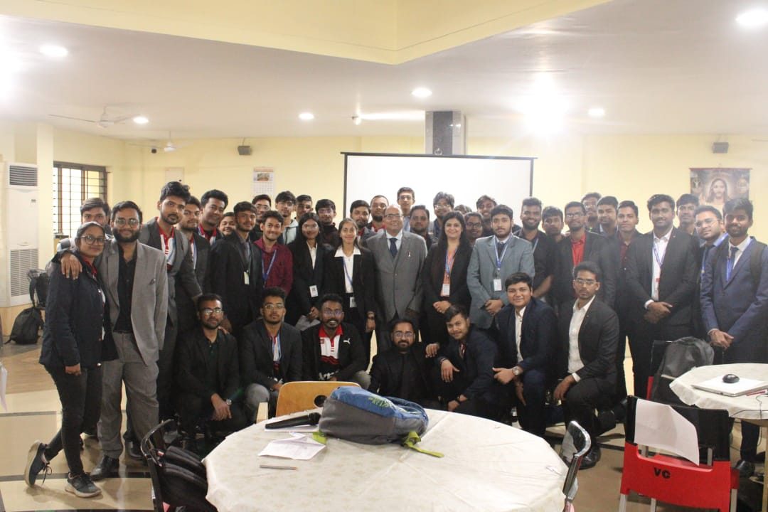 Group photograph of young adults in formal wear with a speaker in front of a projector screen