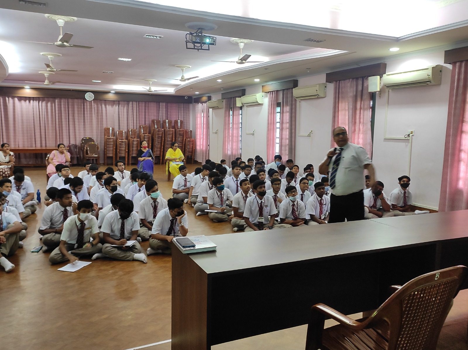 Speaker with a microphone addressing school students seated on the floor of a hall