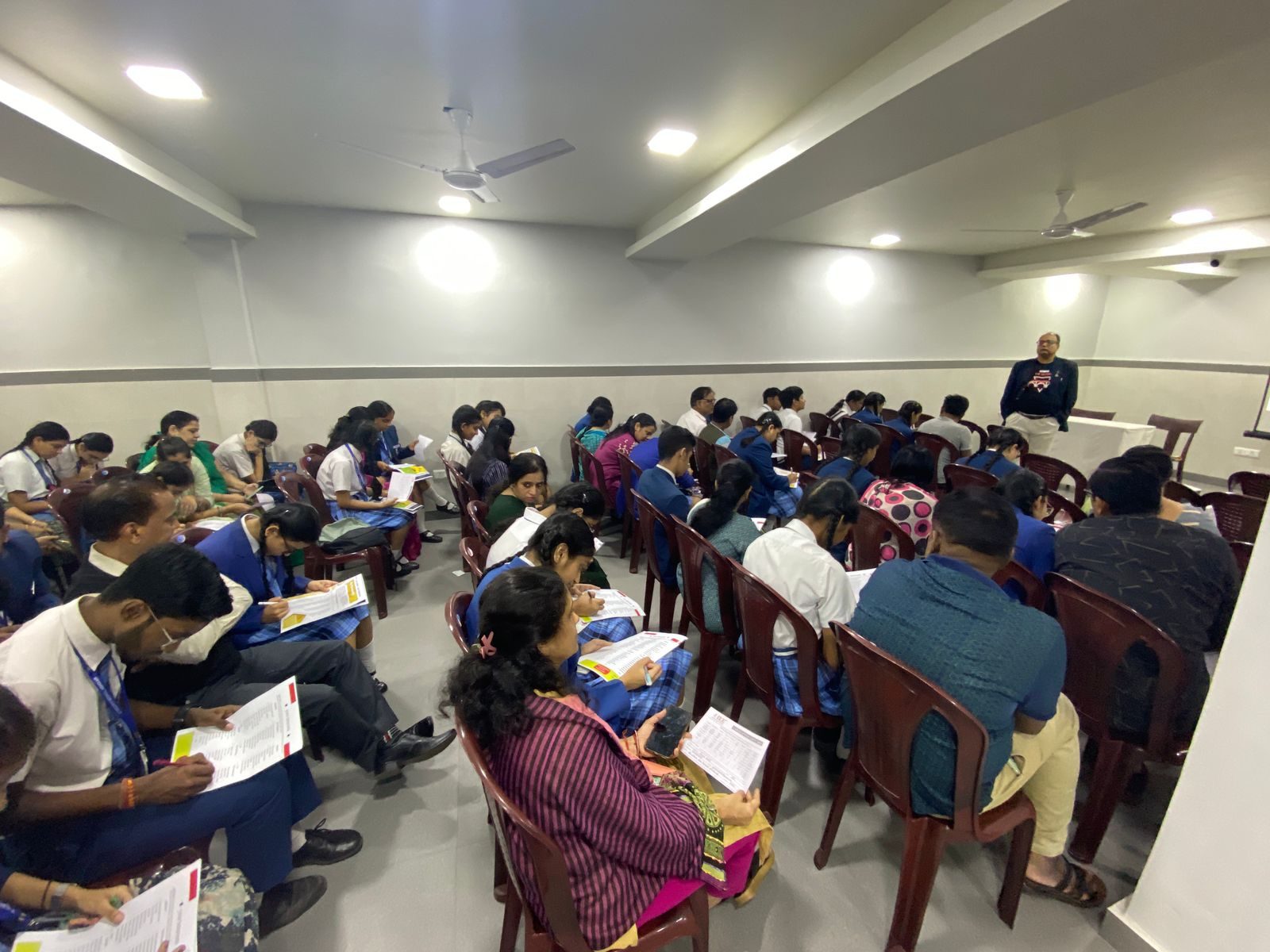 Students and parents filling in sheets during a session while the speaker stands at the front