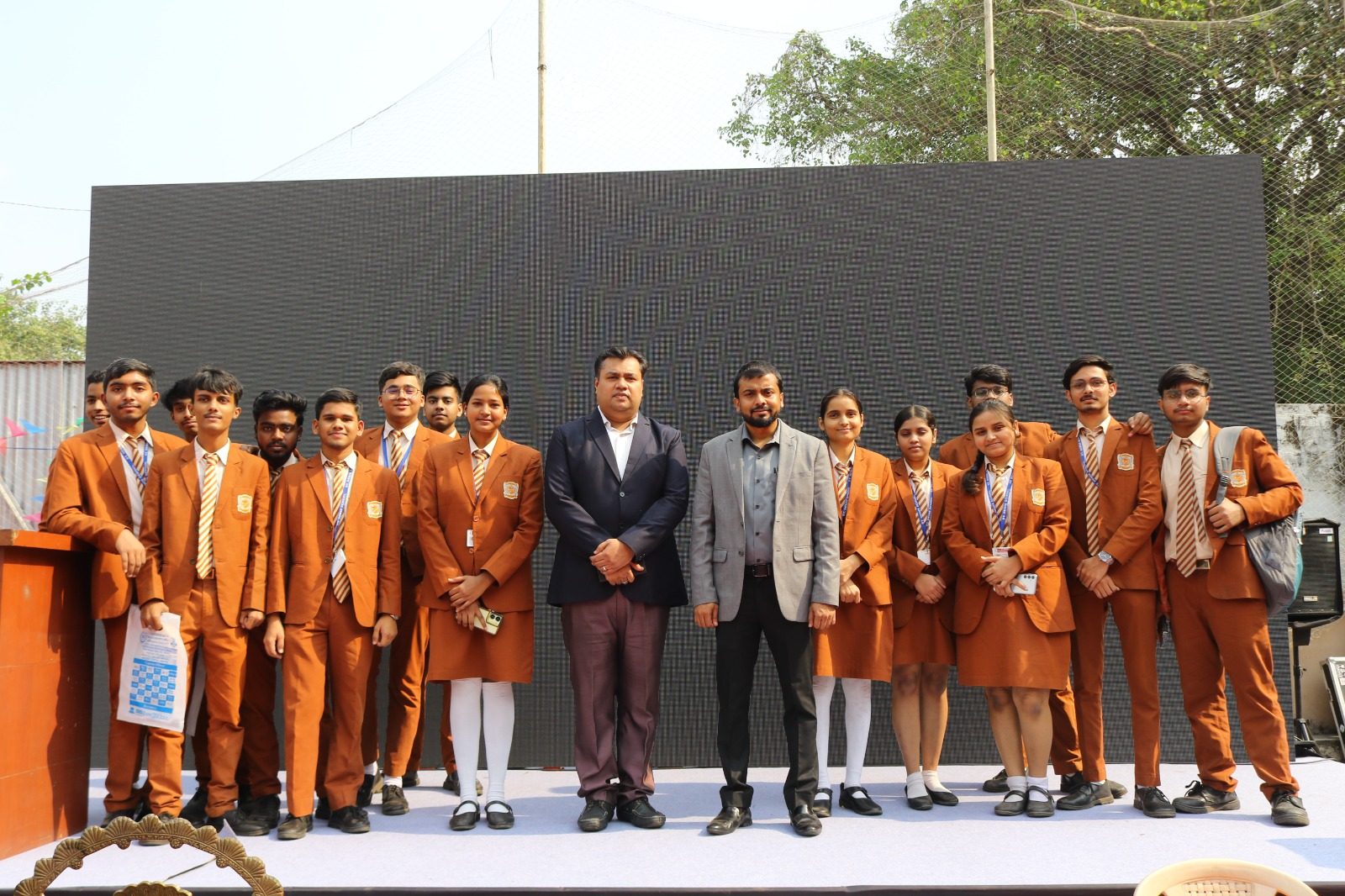 Students in orange blazers posing on stage with two men at a career fair