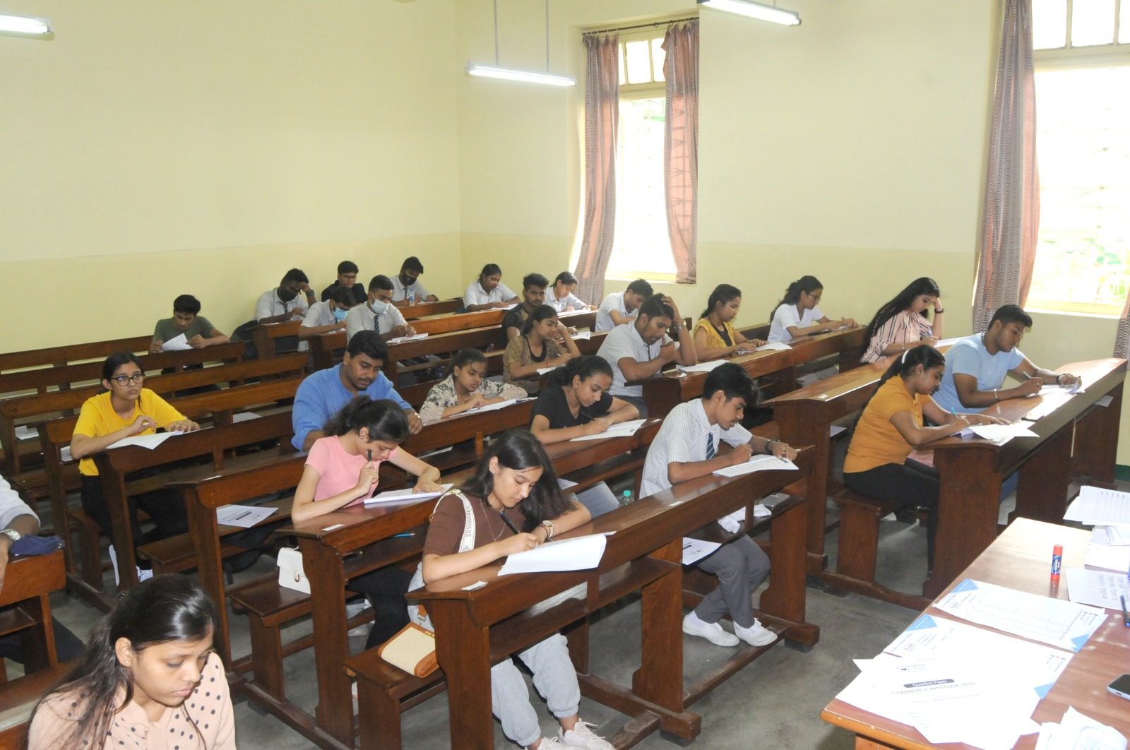 Students writing a test at wooden benches in a classroom