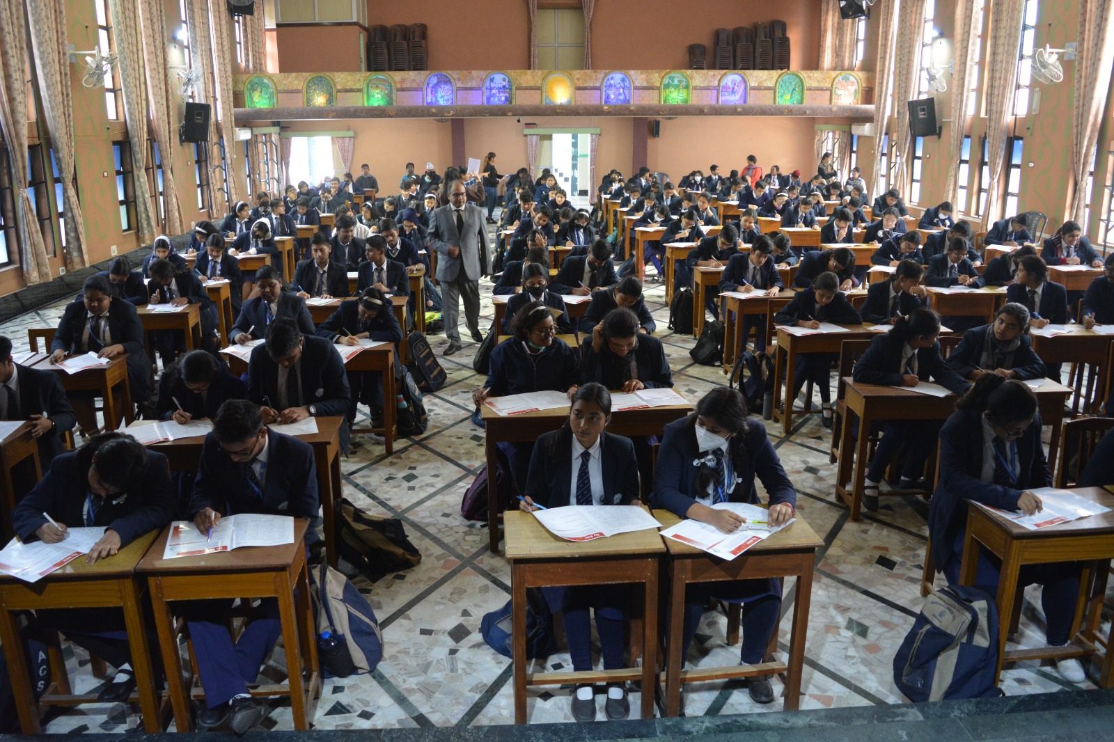Students seated at desks writing a test in a large hall